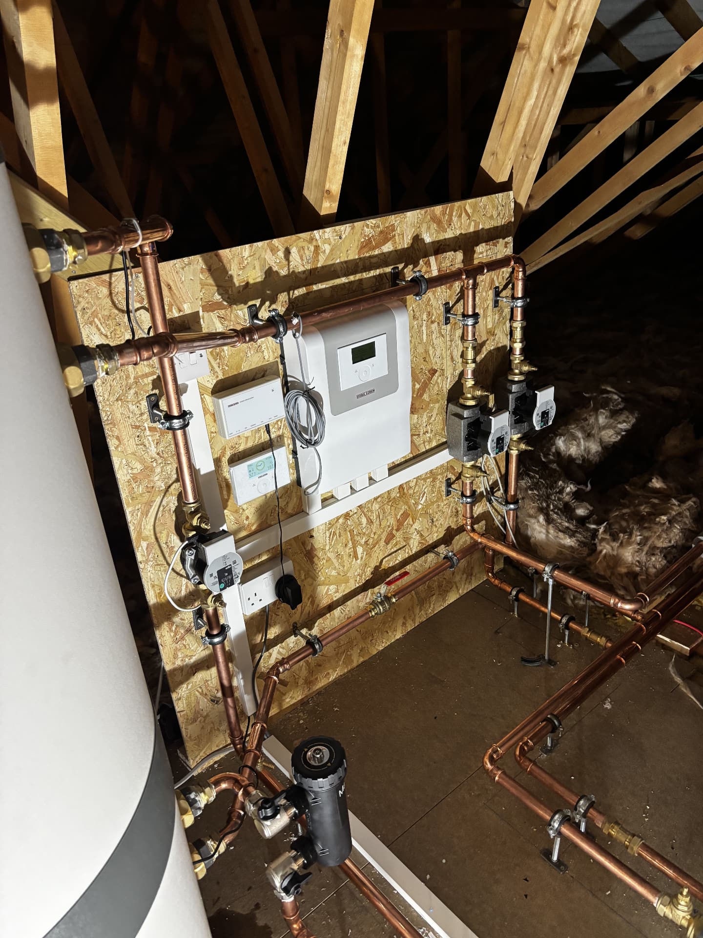 Heat pump pumps, valves and controls fitted on a boarded wall in a loft